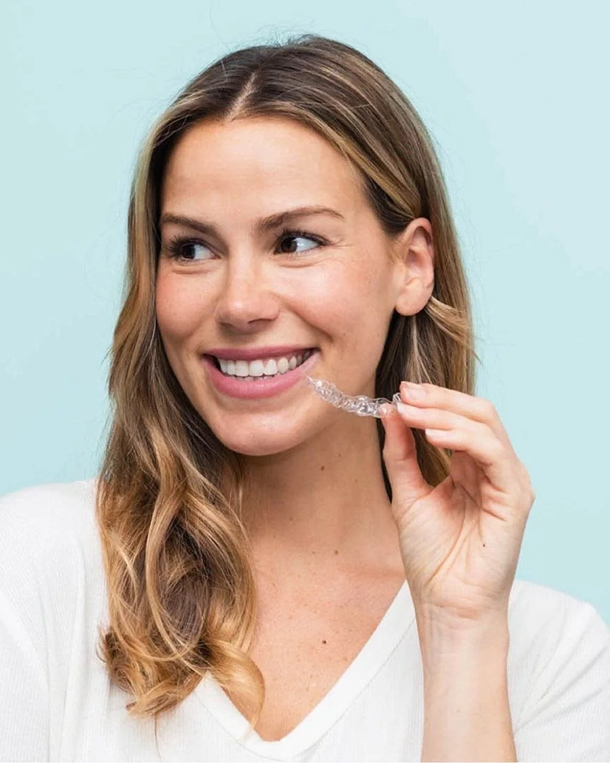 A patient holding her clear aligner beside her smile