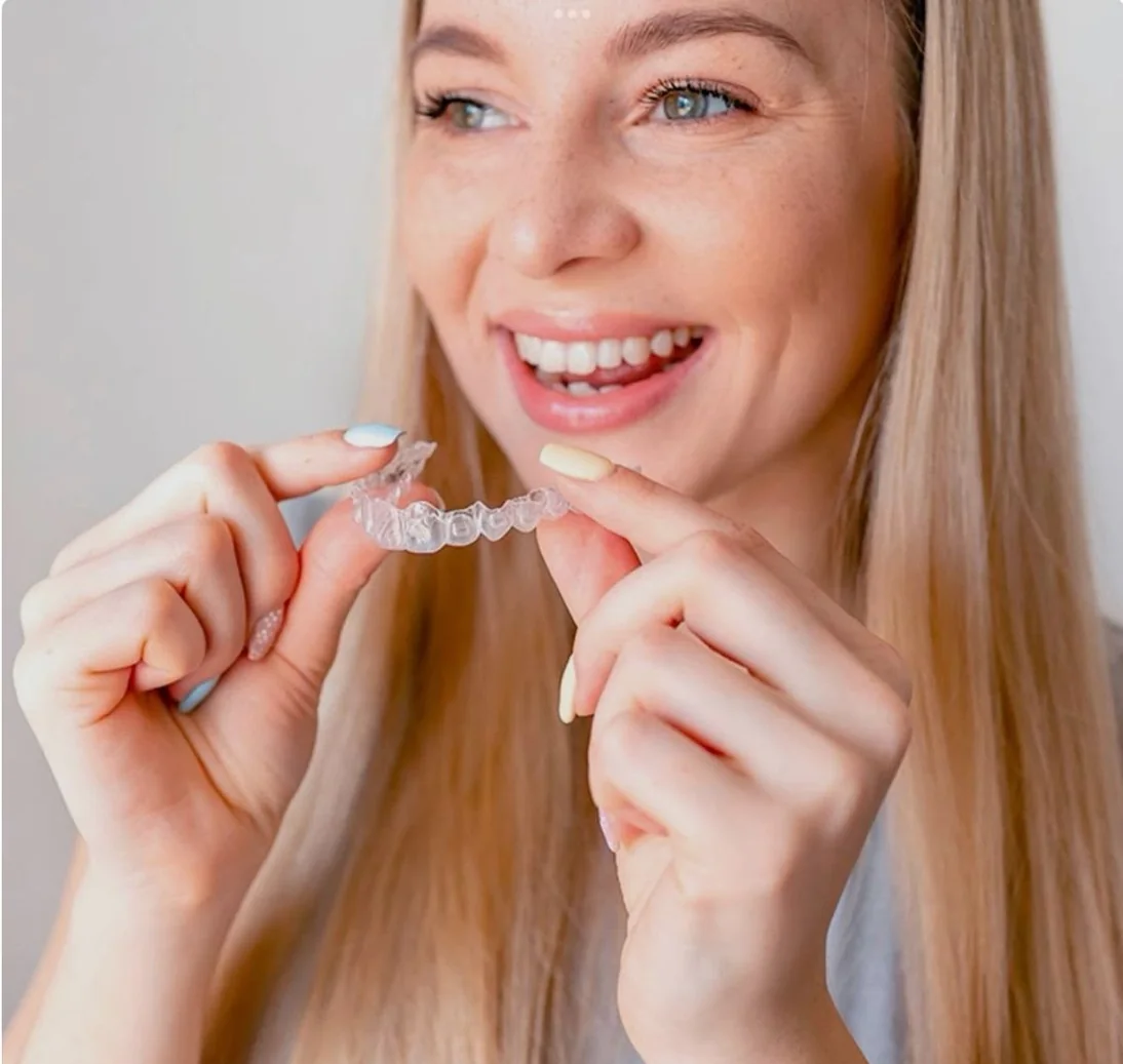 A patient holding her clear aligner below her smile