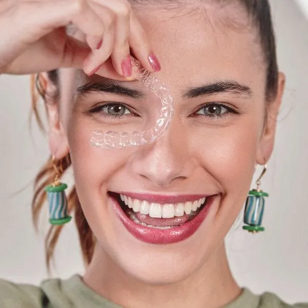 A smiling woman holding a clear aligner
