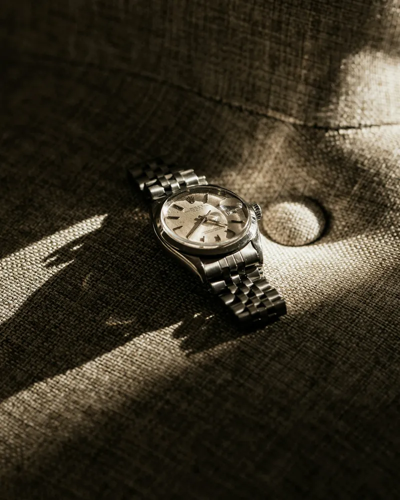 A steel watch on a tufted sofa, in a slice of light