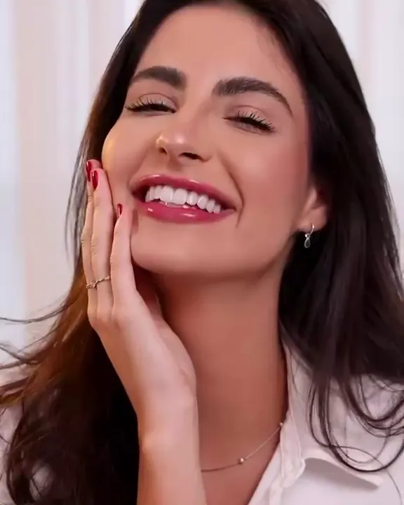 A smiling woman in a white shirt, her hand at her cheek