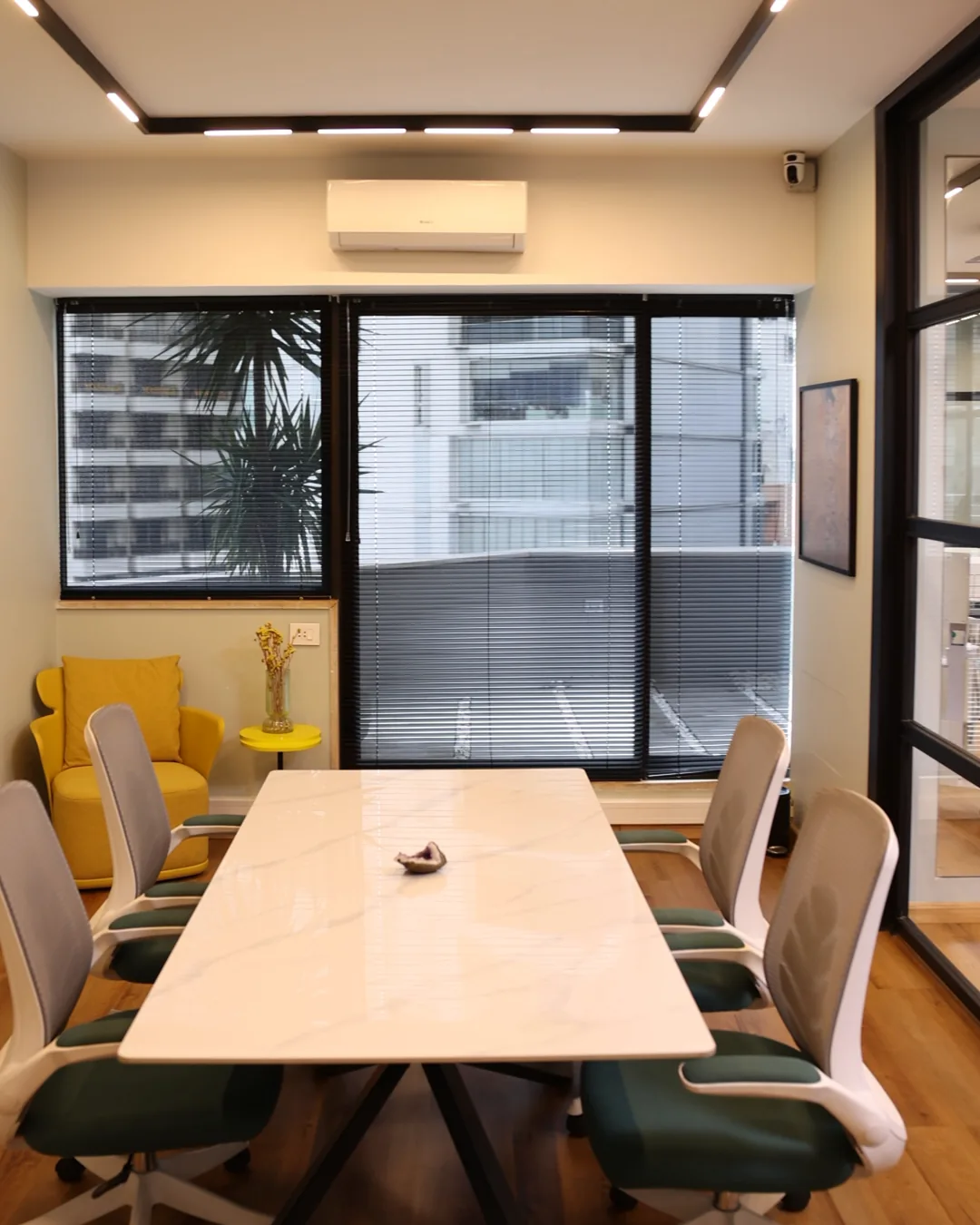 The consultation room: a white marble table, green chairs, a yellow armchair and a window over the city