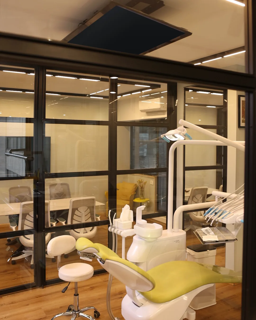 A treatment room with a lime-green chair, seen through a black-framed glass wall